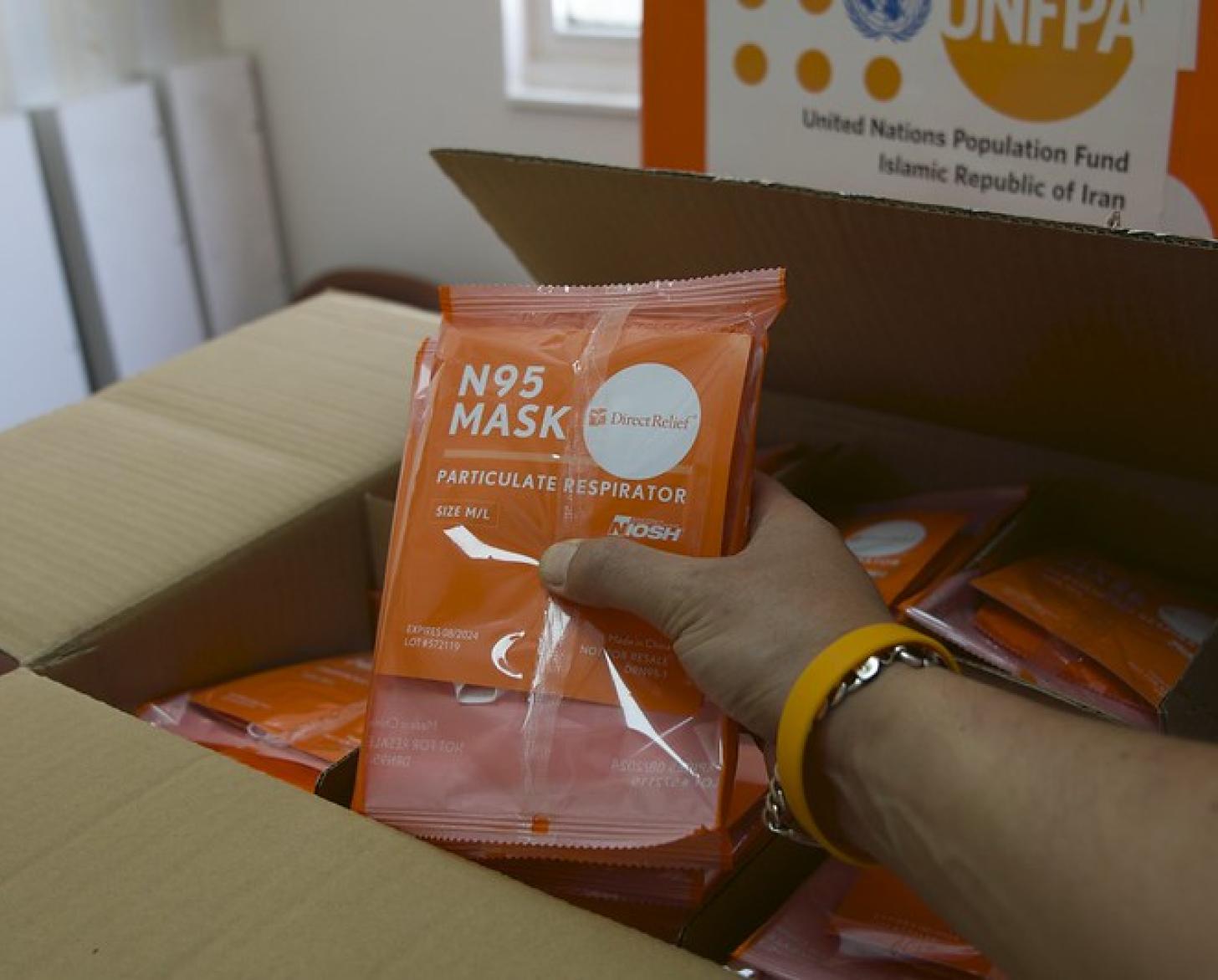 Una mano sostiene un paquete de EPP sobre una caja donada por el UNFPA.