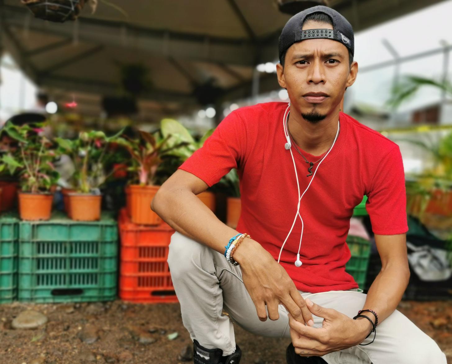 يركع خوان كارلوس على الأرض تحت خيمة وأمام صف من النباتات.