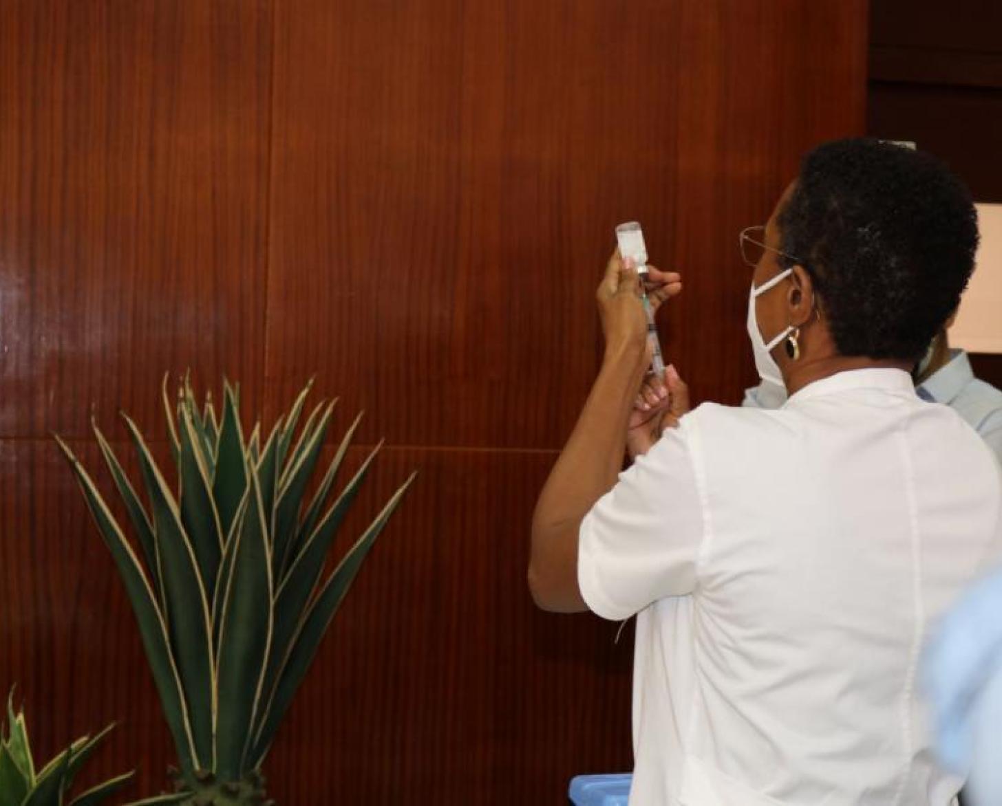 ممرضة تقف بعيدًا عن الكاميرا أثناء تحضيرها للجرعة الأولى من لقاح فيروس الورم الحليمي البشري.