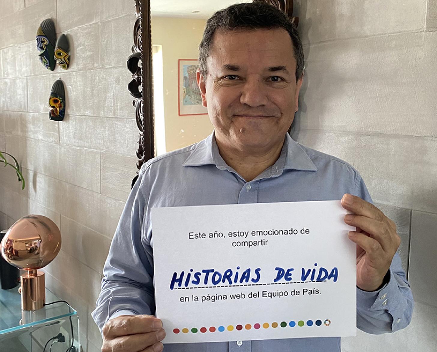 A man smiles sweetly at the camera as he holds up a small sign that shares his vision of the site for the next year, in Spanish.