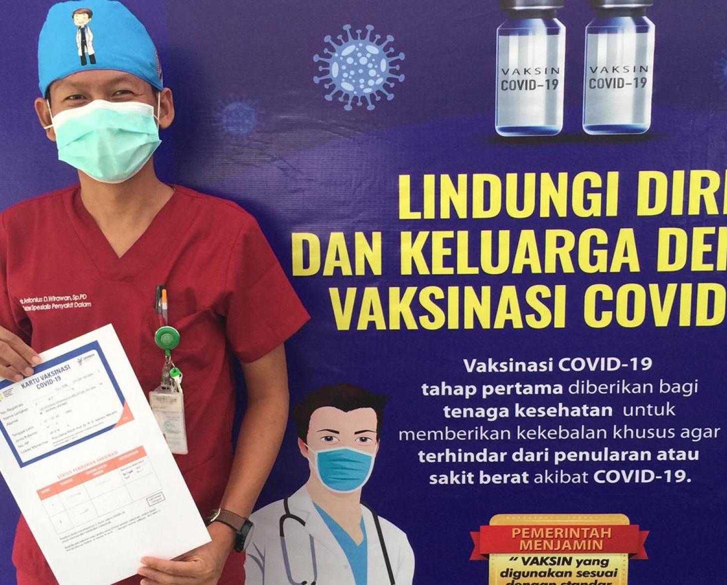 Dr Antonius Irawan stands in front of a COVID-19 vaccination poster holding his COVID-19 vaccination certificate after he received his first dose of COVID-19 vaccine at Dr Kandou District General Hospital .in Manado City, North Sulawesi Province
