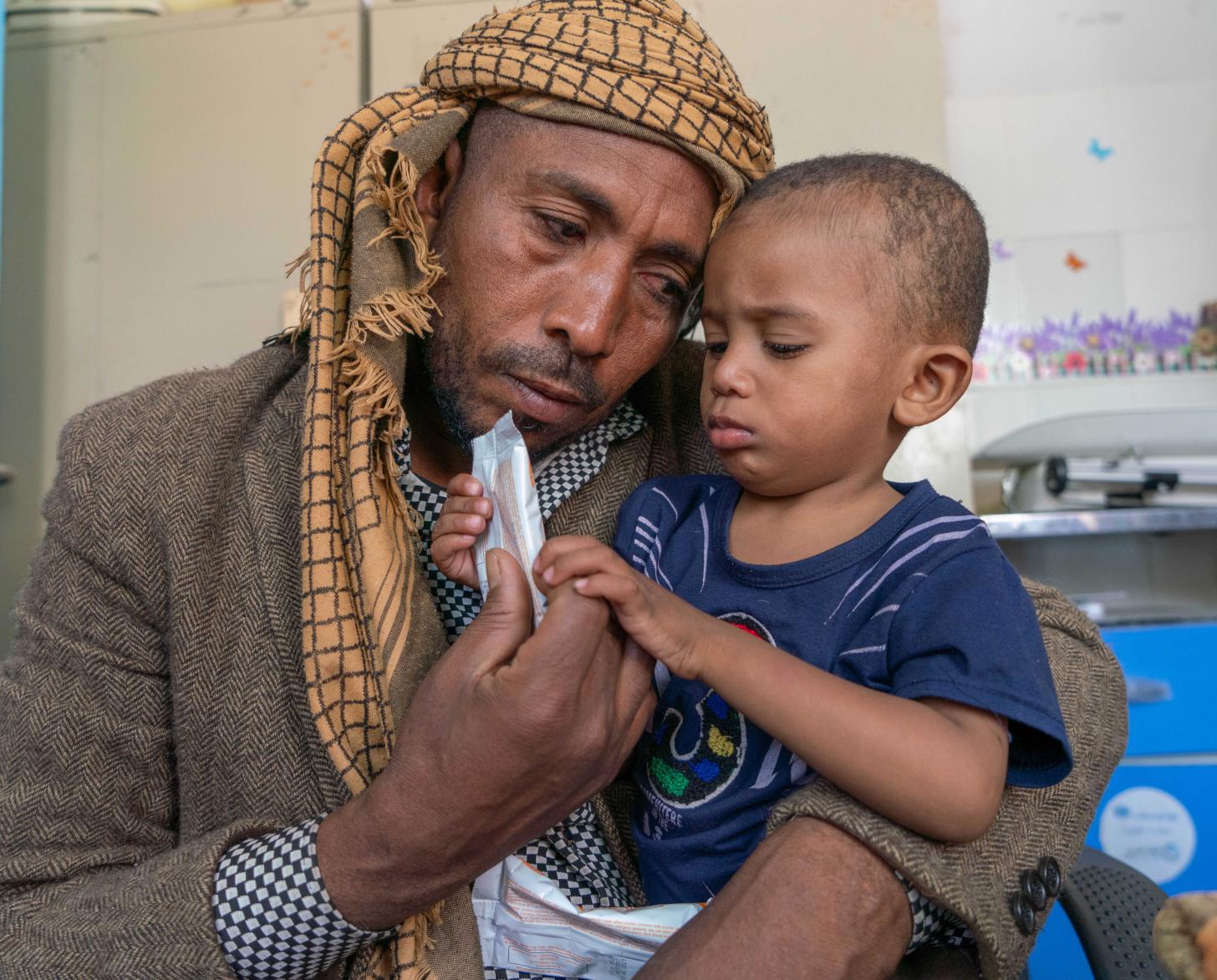 Sultan (1 year and 9 months) who suffers from moderate malnutrition receives nutrition supplies (Plumpy sup) at WFP supported health clinic in Amant Al Asimah with his father, Arafat (37), who is lovingly looking at his son. 