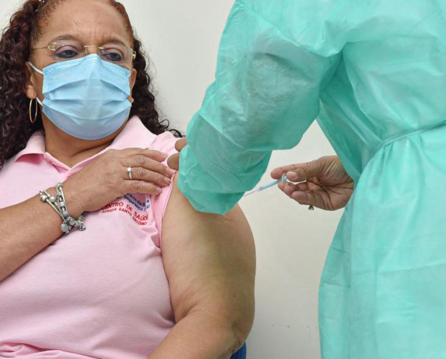 Nurse, Helga Fontes, rolls up her sleeve as a healthcare worker injects her with the COVID-19 vaccine.