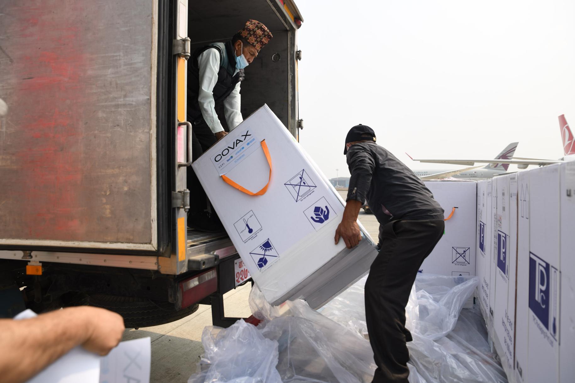 Two men load large white boxes into a truck. 