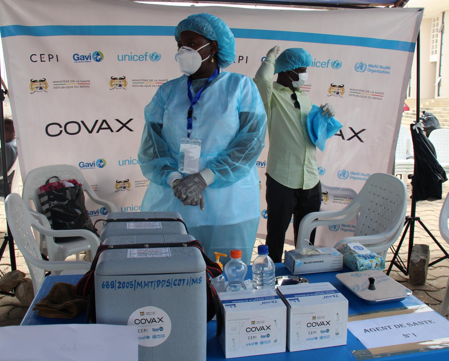 Dos personas con equipo médico de protección se paran cerca de los suministros de vacunación.