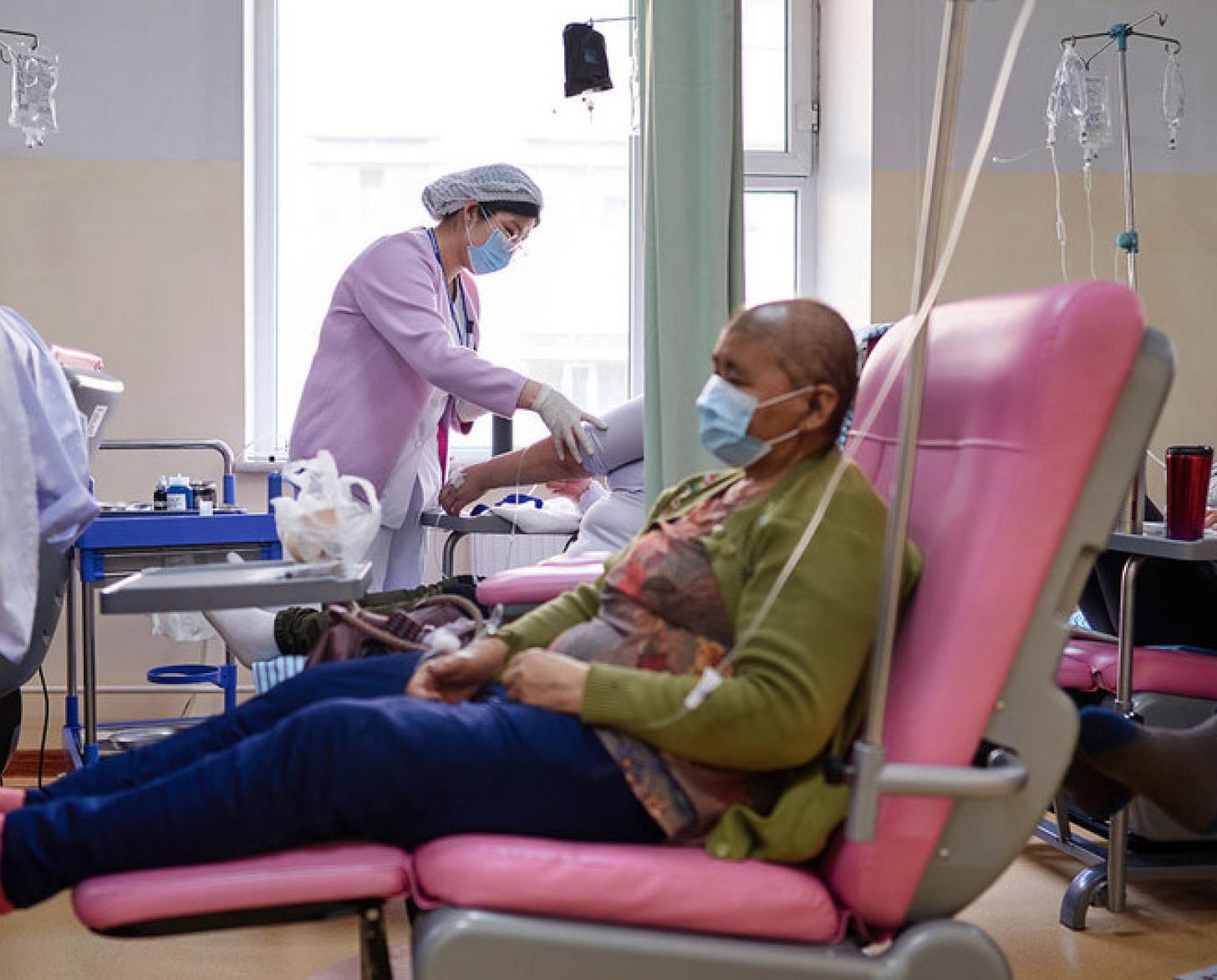 In a medical office a person is sits in a pink chair receiving medicine via an IV.