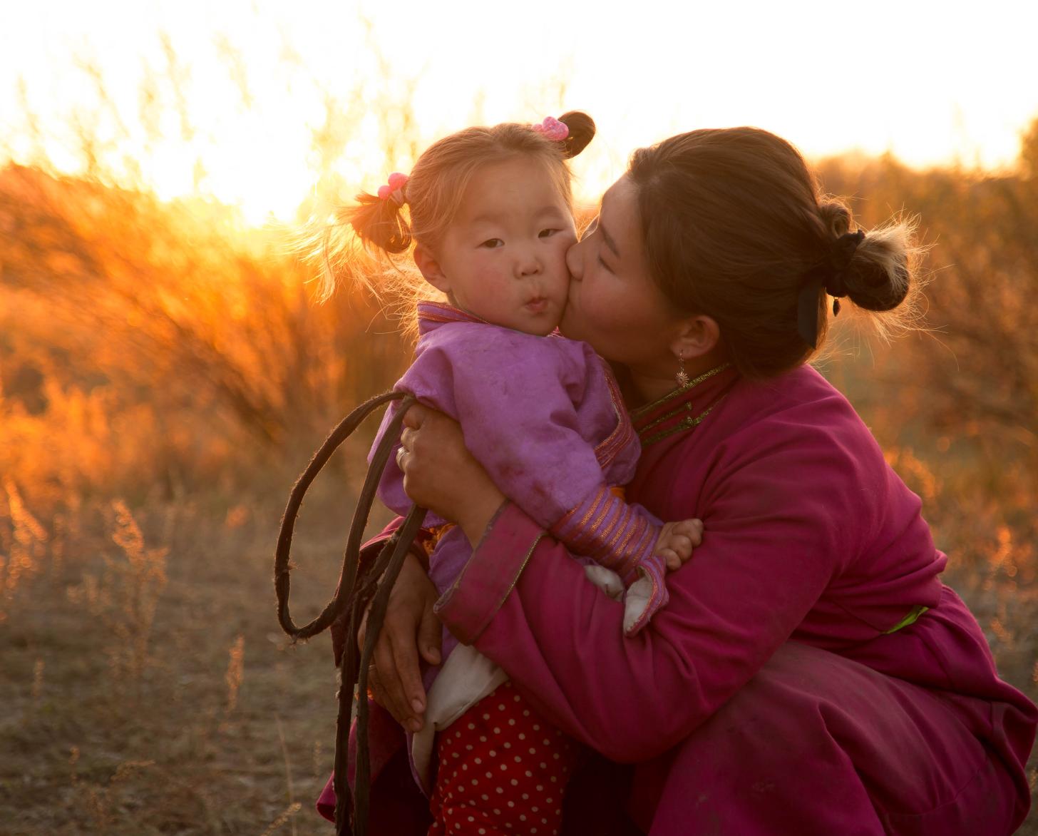 一名妇女在田野里亲吻一个年轻女孩的脸颊。