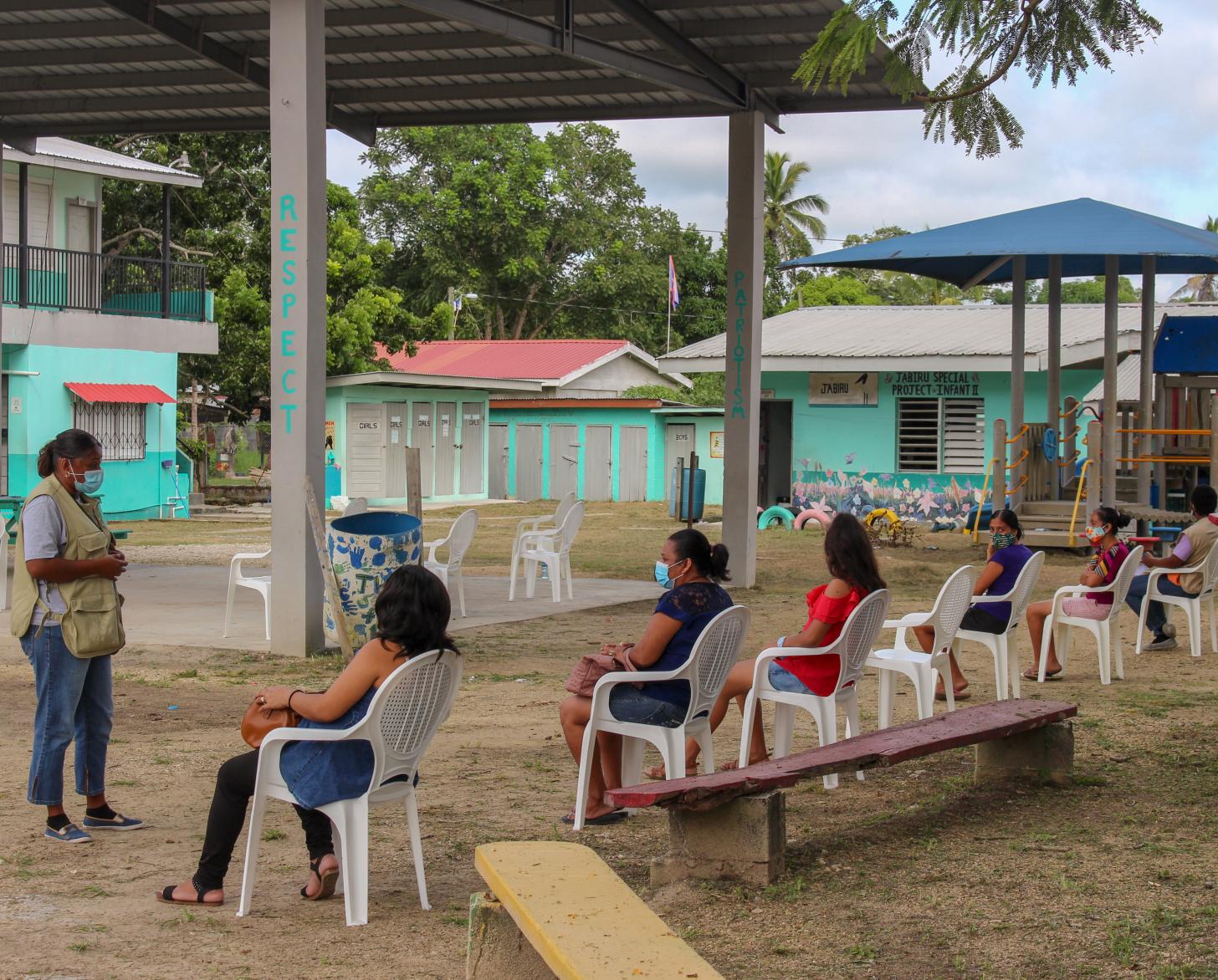 A group of socially distanced women listen to a speaker standing in front of the group.