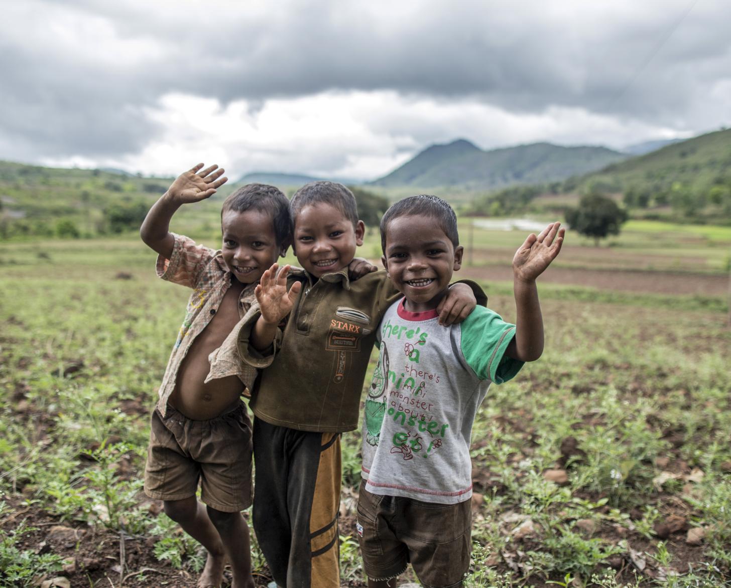 En una planicie vegetal, tres pequeños sonrientes saludan a la cámara.