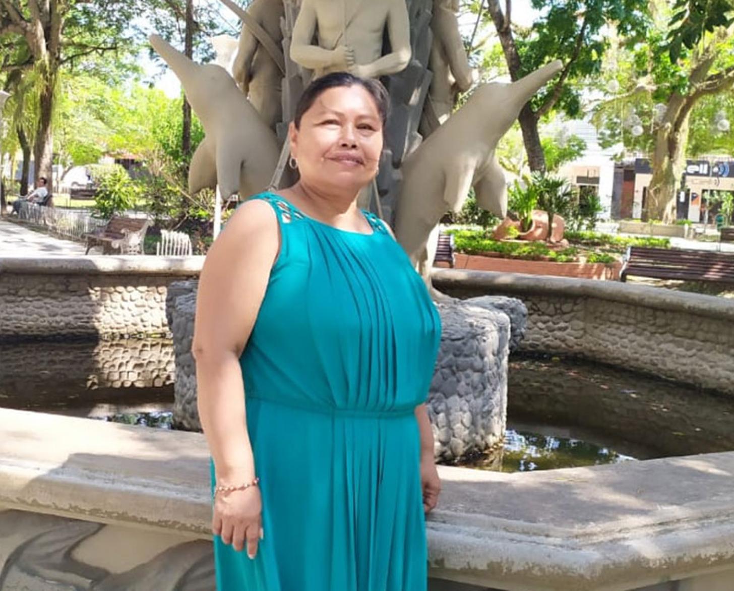 A woman in a teal dress stands in front of a fountain. 