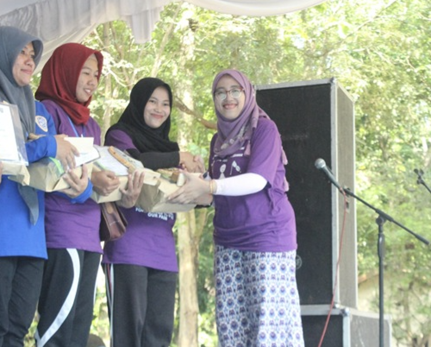 Four women in hijabs smile at the camera as they receive packages. 