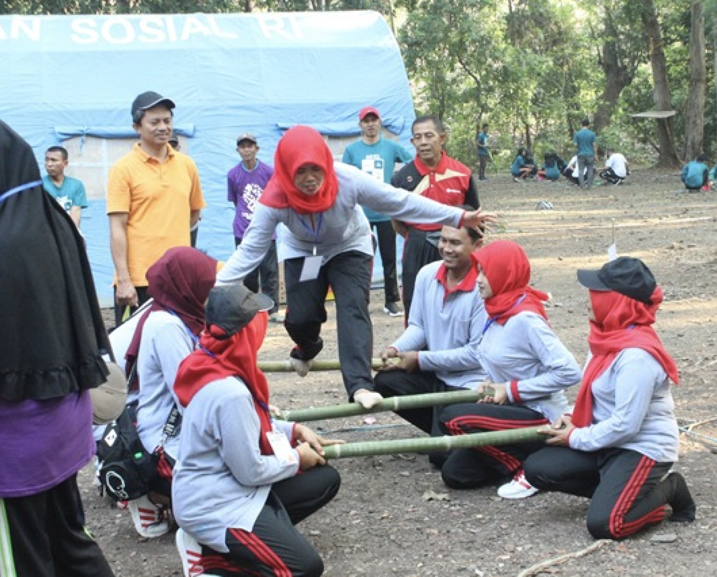 A group of several people play games with sticks in clearing near a wooded area. 