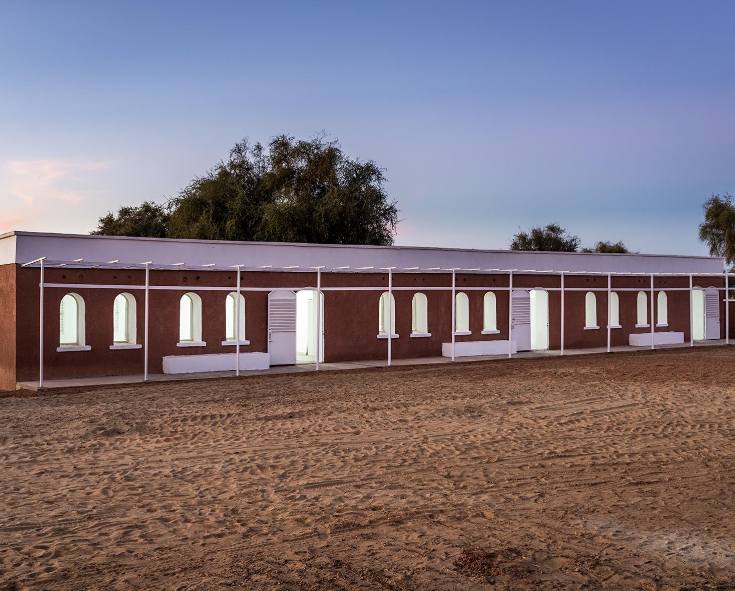 Édifice d'une école construite en terre crue, illuminée de l'intérieur à la tombée de la nuit.