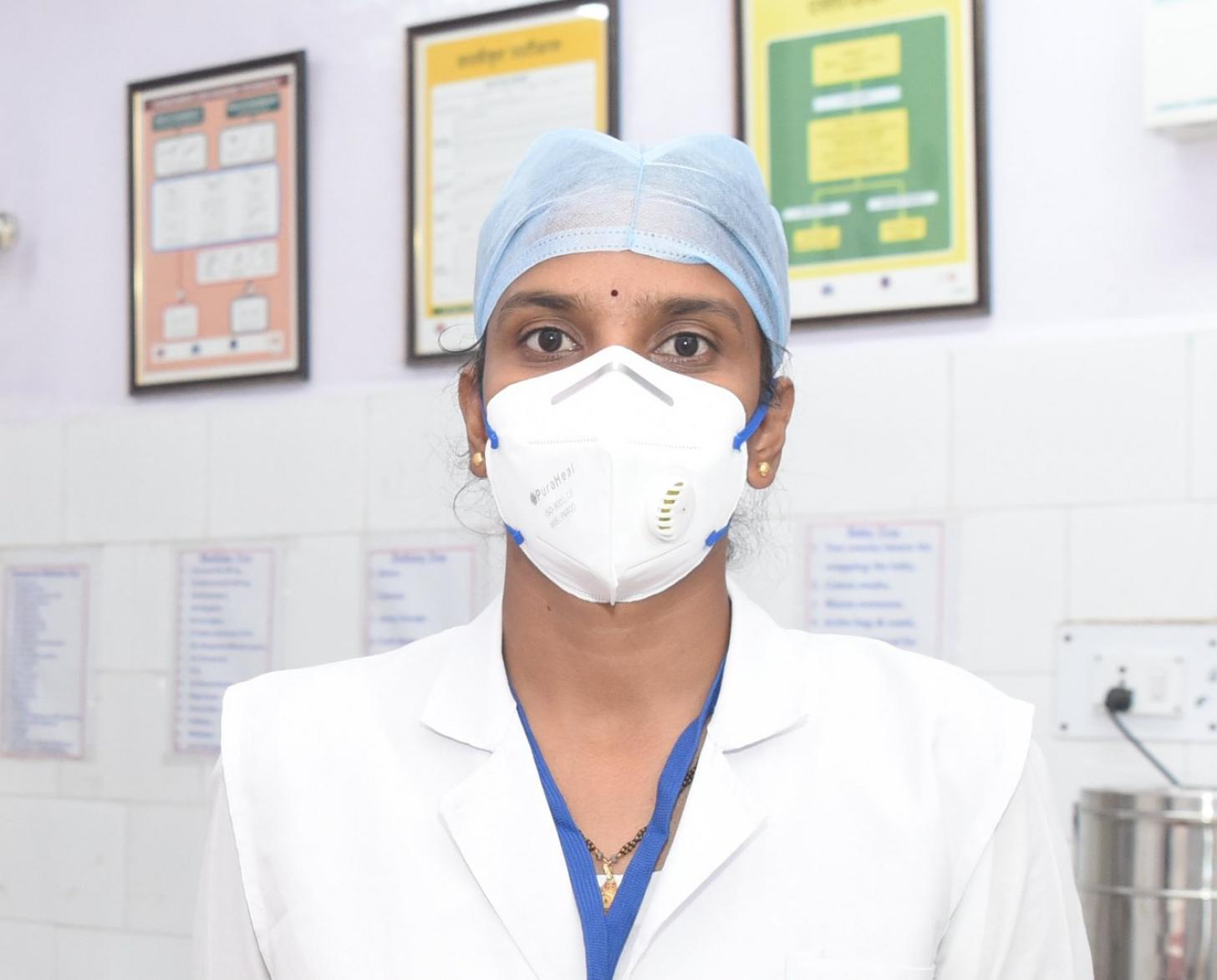 A medical professional in a white face mask looks at the camera from a medical office.