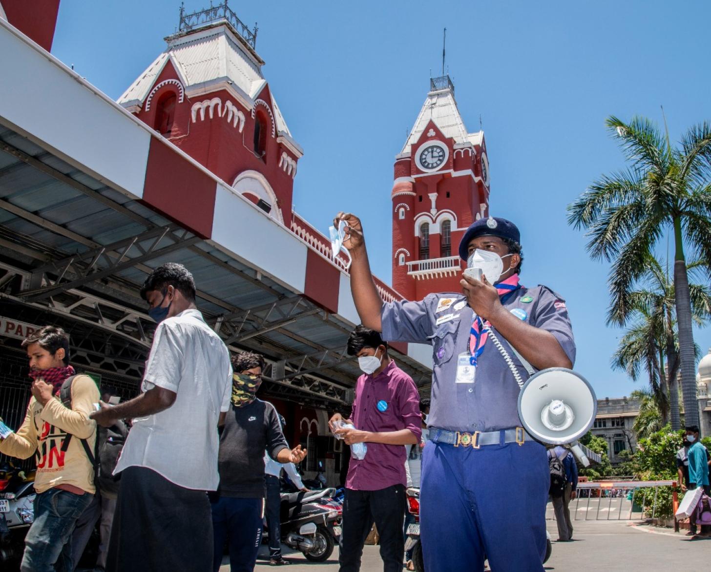 A man with a bullhorn speaks outside a red building on a nice day. 
