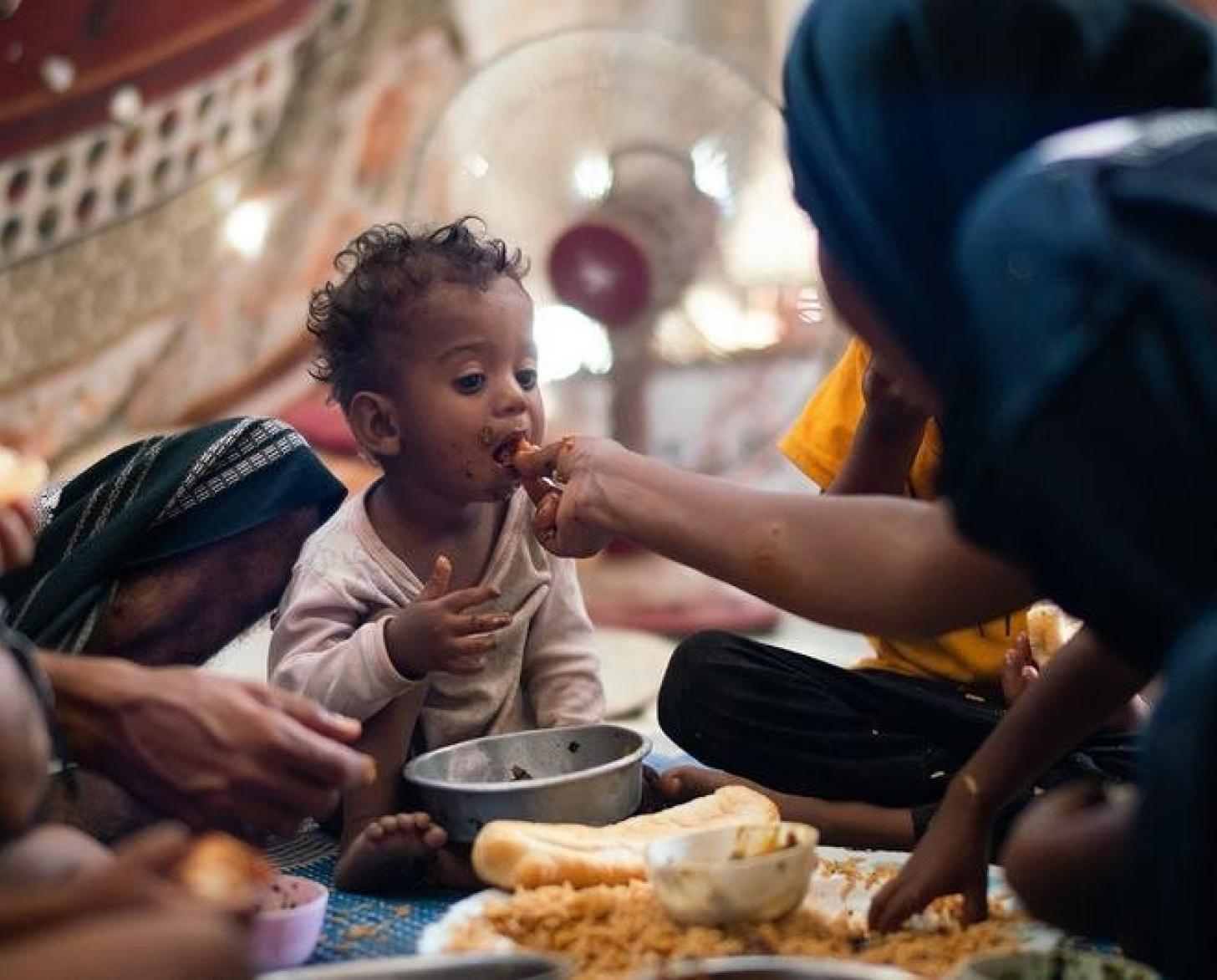 Un niño de un año come con su familia en un campamento de desplazados internos en Adén, Yemen.
