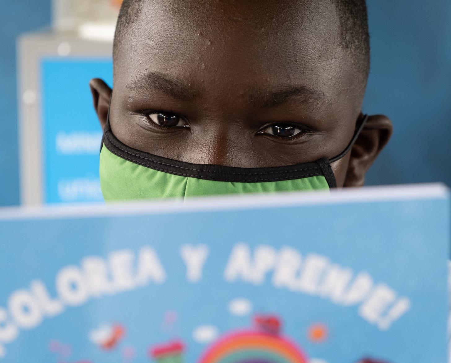 Portrait en gros plan sur une jeune garçon portant un masque de protection respiratoire vert et concentré sur la lecture d'un livre.