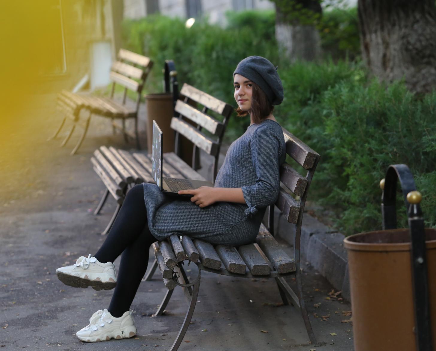 شابة تجلس على مقعد في حديقة مع جهاز حاسوب محمول.