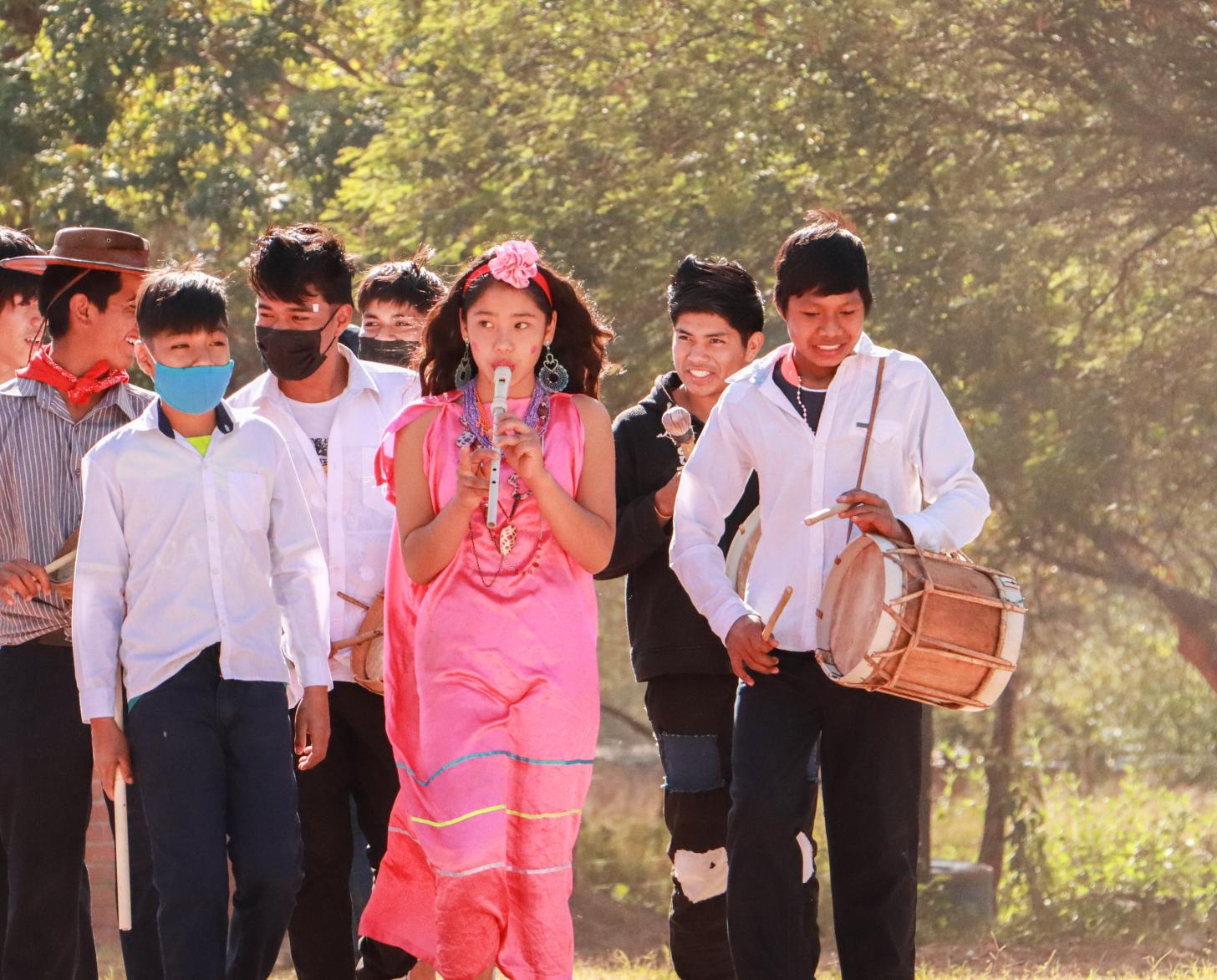 Un grupo de jóvenes parte del proyecto de escuelas resilientes en Bolivia tocan música tradicional guaraní en un área verde.