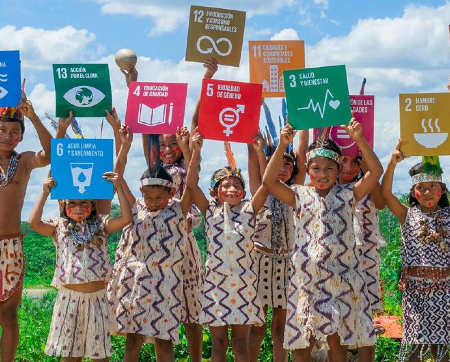 En un área verde, un grupo de niños y niñas sostienen en alto carteles de los Objetivos de Desarrollo Sostenible.