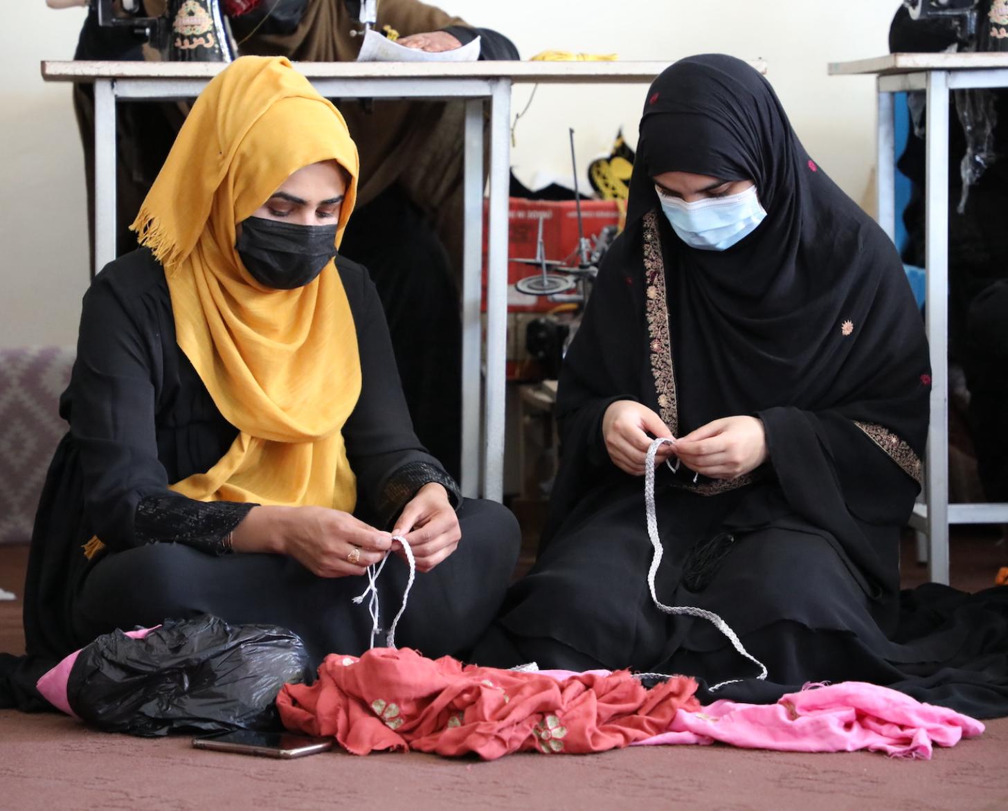 سيدتان محجبتان تجلسان على الأرض تتعلمان مهارات الخياطة