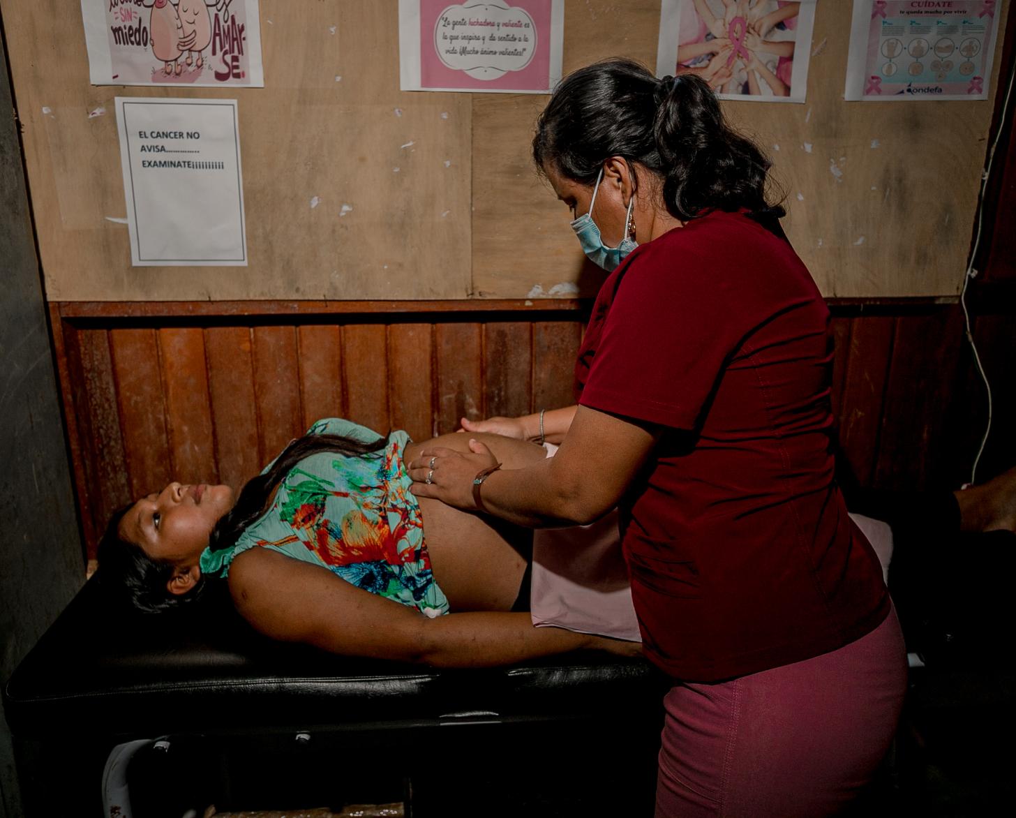 Personal sanitario auscultando a una paciente que se encuentra acostada sobre una camilla negra.