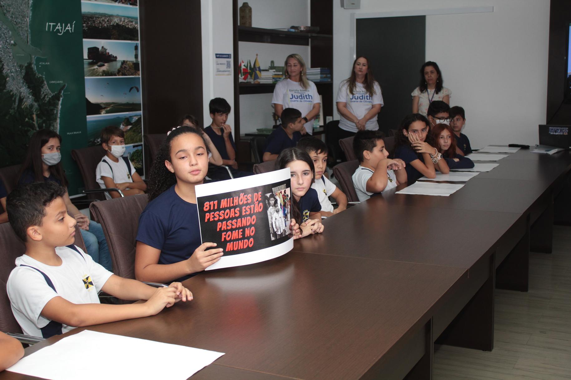 在伊塔贾伊市政厅的市长办公室举行的特别表彰活动中，一群孩子正和他们的老师坐在会议室里。