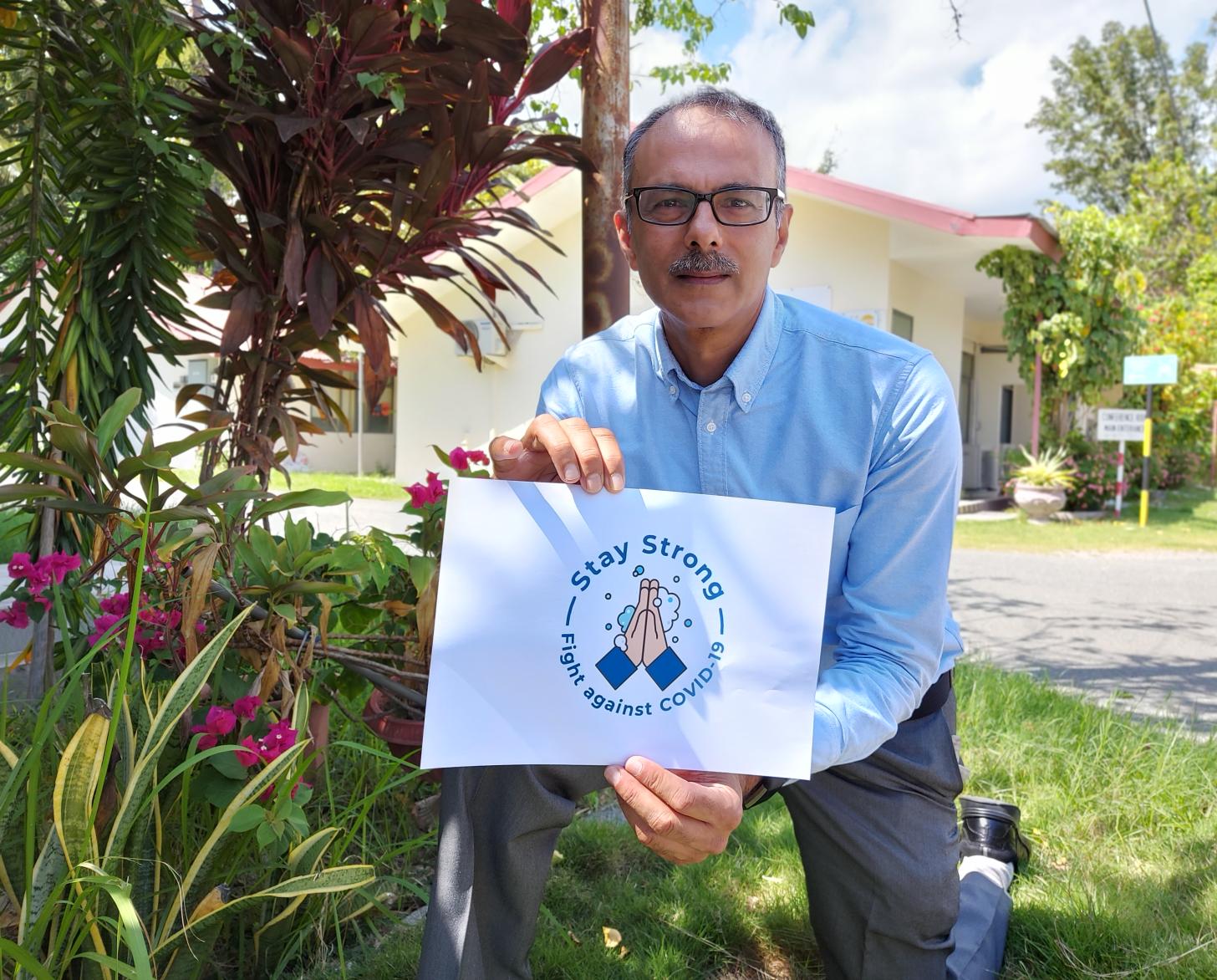 El Coordinador Residente saliente de Timor-Leste, Roy Trivedy, se arrodilla con un cartel para fomentar el lavado de manos durante la COIVD-19.
