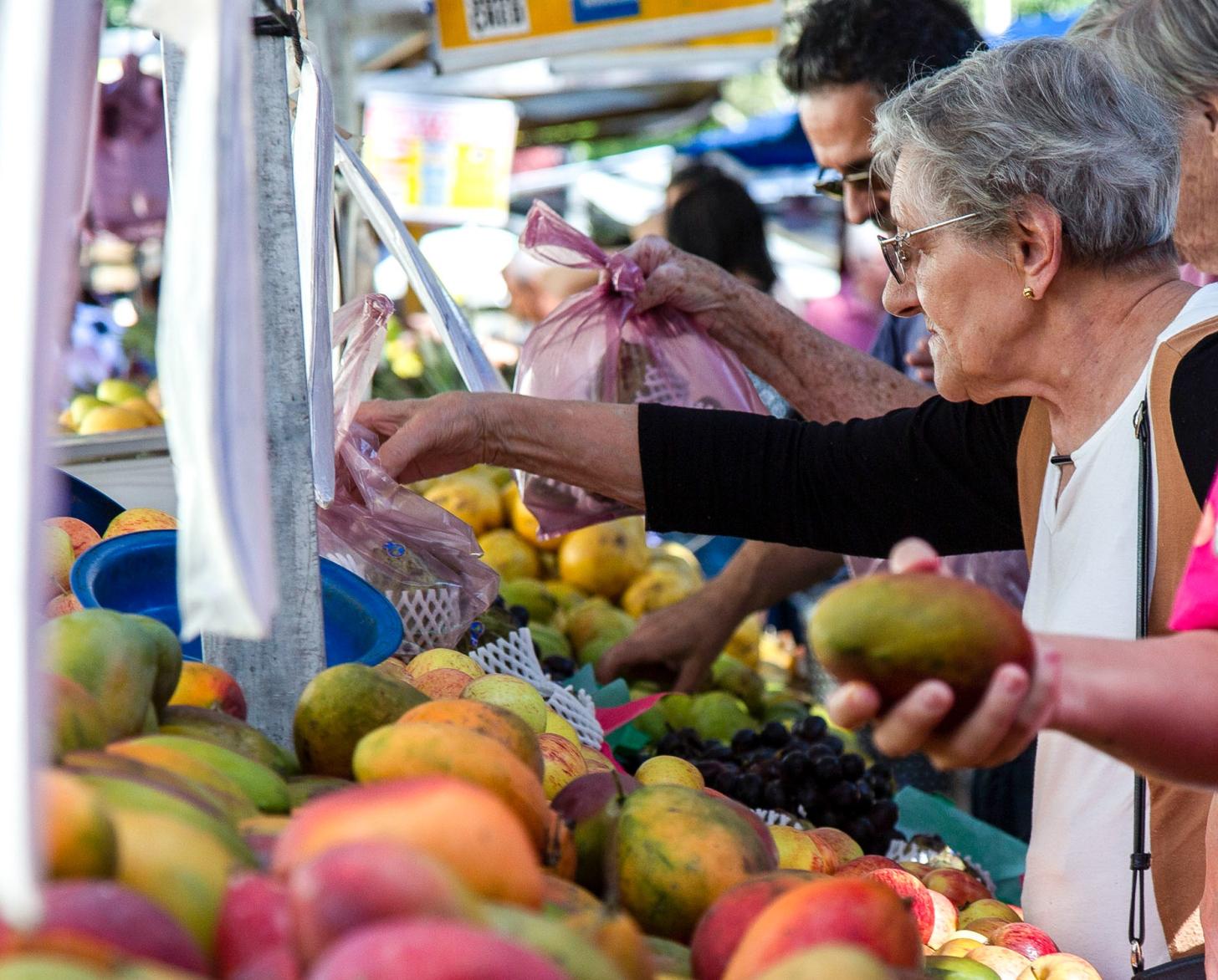 woman in market reaches for bag of pears