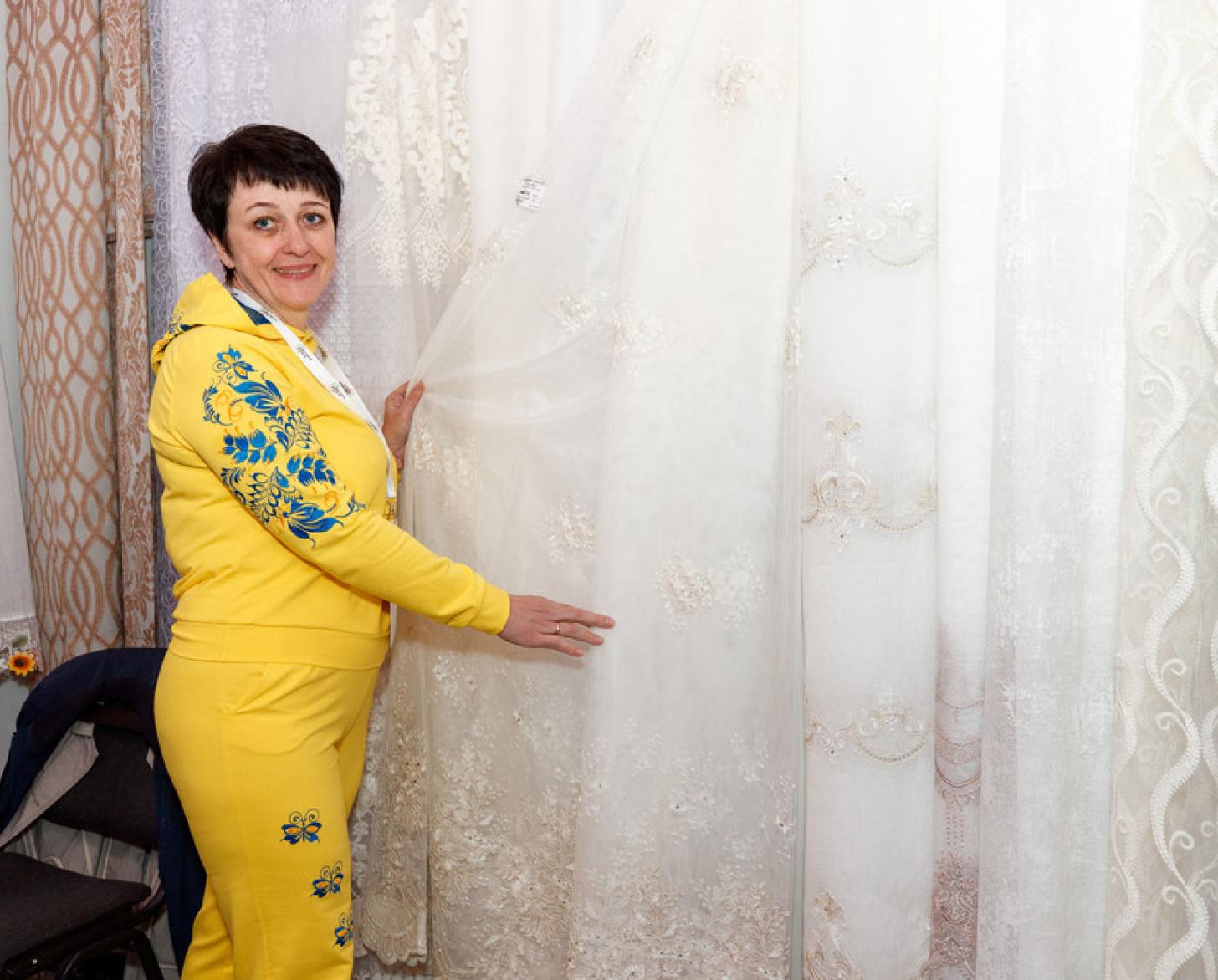 Женщина в желтом костюме стоит около стенда с тюлями на выбор
