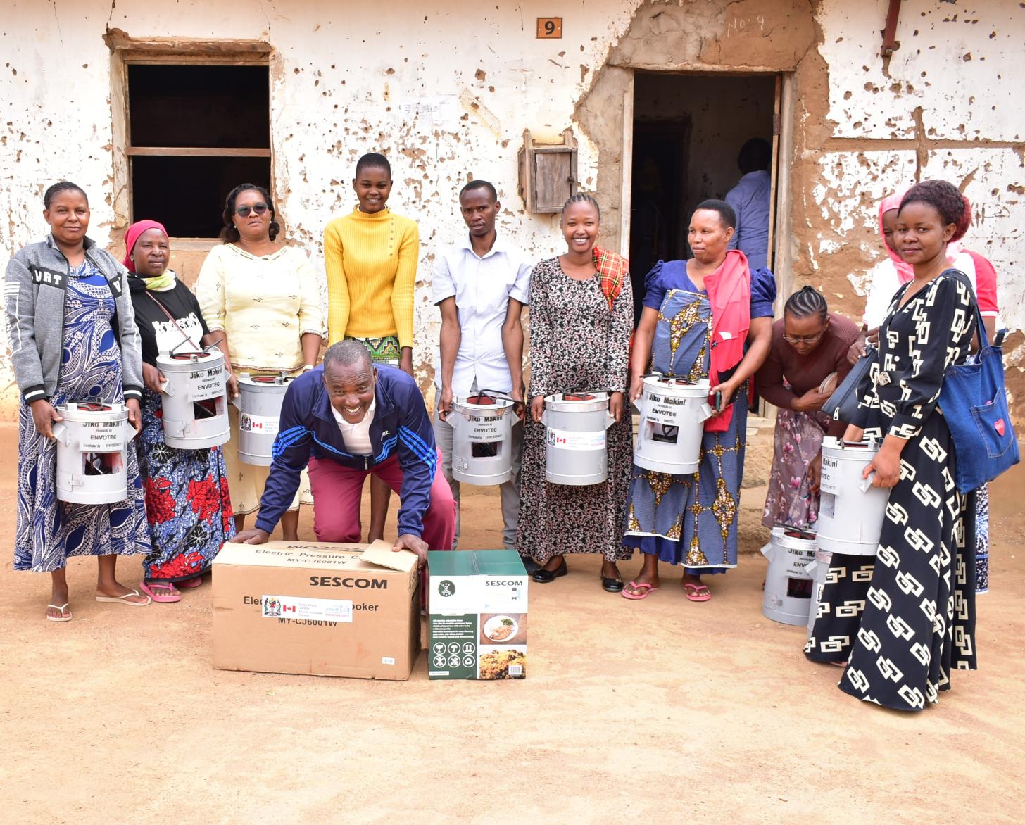 A group of women in a semi-circle and a man in the center hold small energy-saving stoves. 
