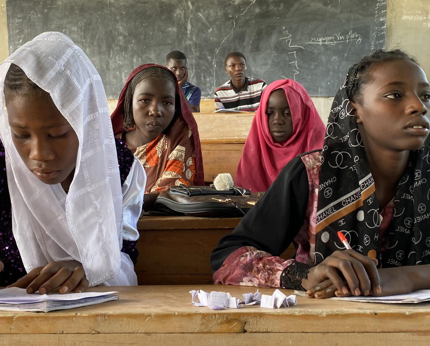A group of four girls reading and writing on school benches in a classroom