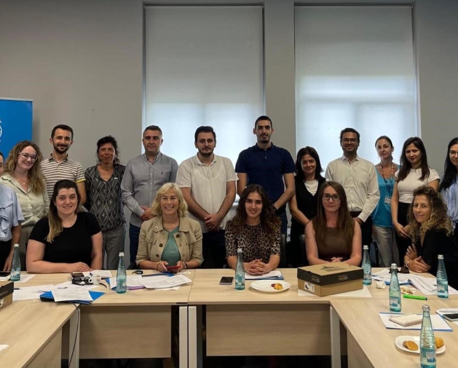 A group of people looking at the camera and smiling in an indoor setting with UN branding in the background