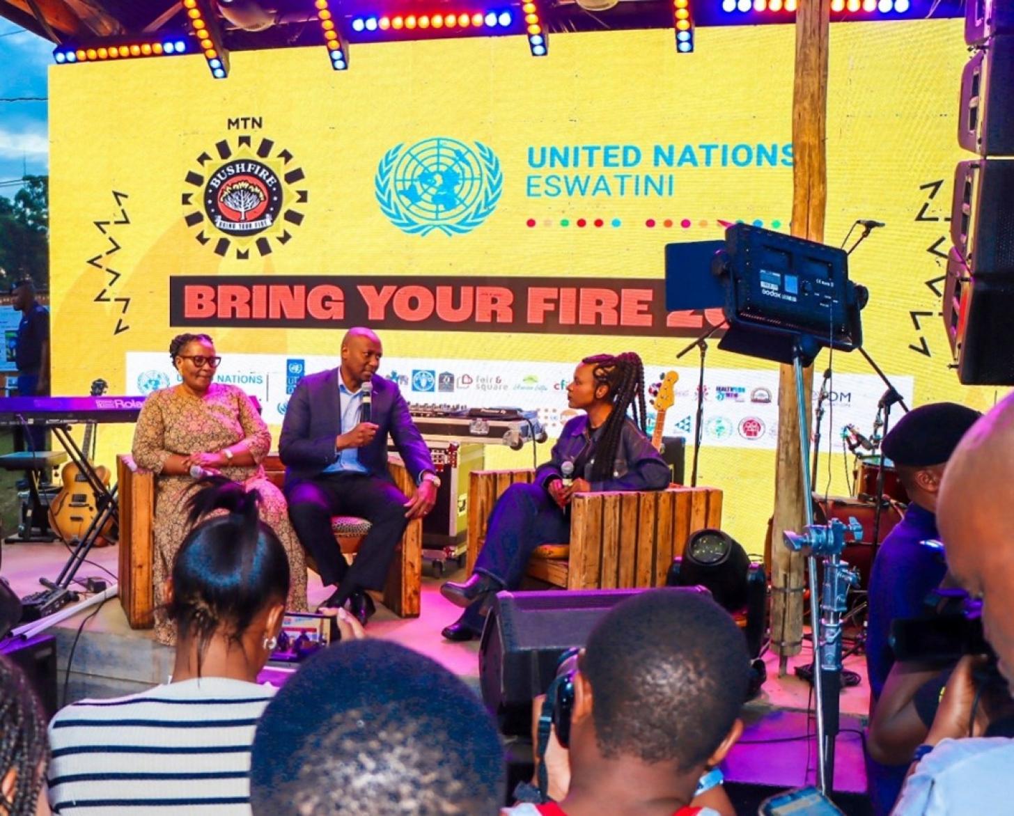 A group of three panelists discuss on stage in front of an audience