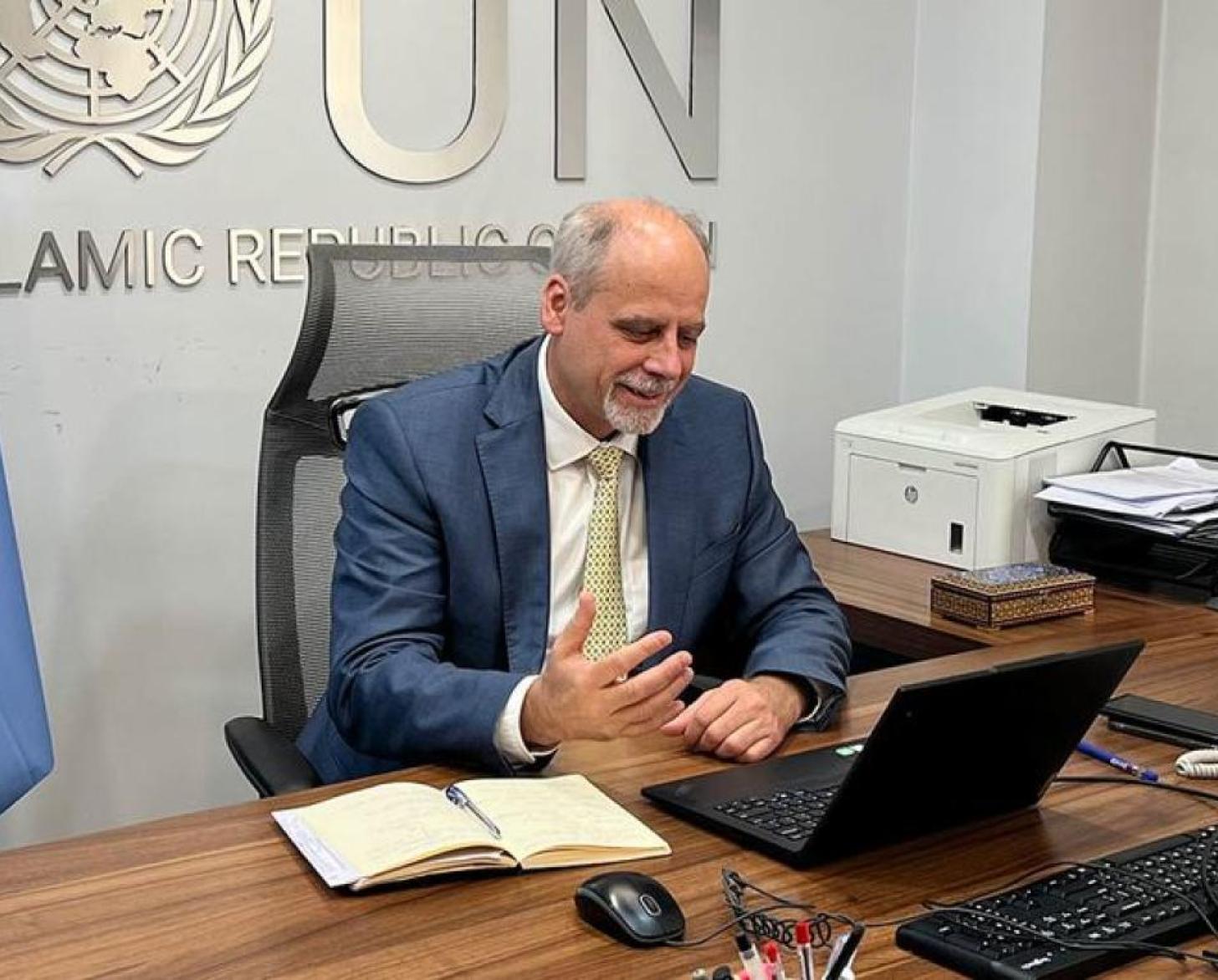UN Resident Coordinator sits at a desk with the UN flag behind him