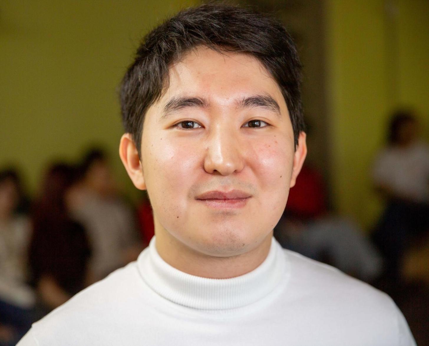 A man looks at the camera and smiles, he is wearing a white top