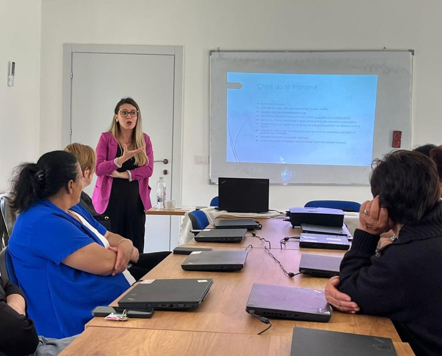 A woman in Albania gives a training session in front of other women in a small room.