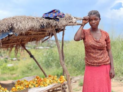 A girl in a pink dress stands by a straw hut