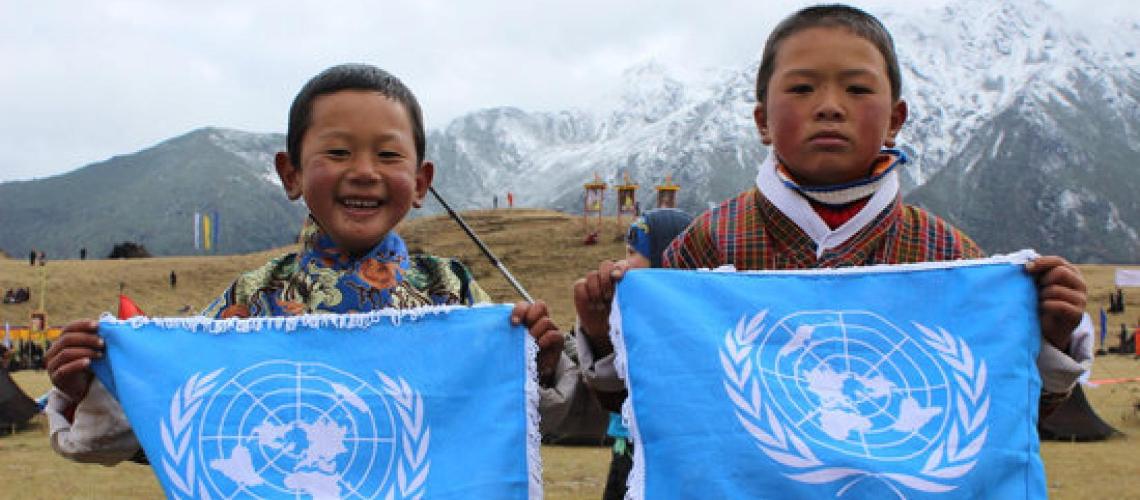 Two young boys hold the United Nations flag while looking directly at the camera. 