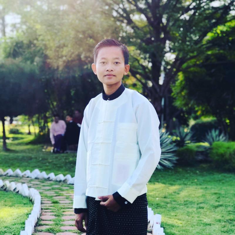 Retrato de medio cuerpo de Min Min, activista de los derechos LGBTQI, quien mira con determinación a la cámara, en un área verde.