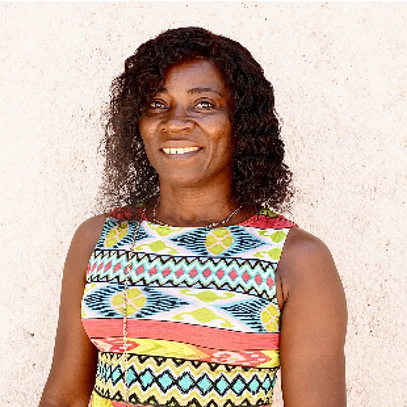 Una mujer con una colorida blusa, de colores brillantes, sonríe a la cámara. 